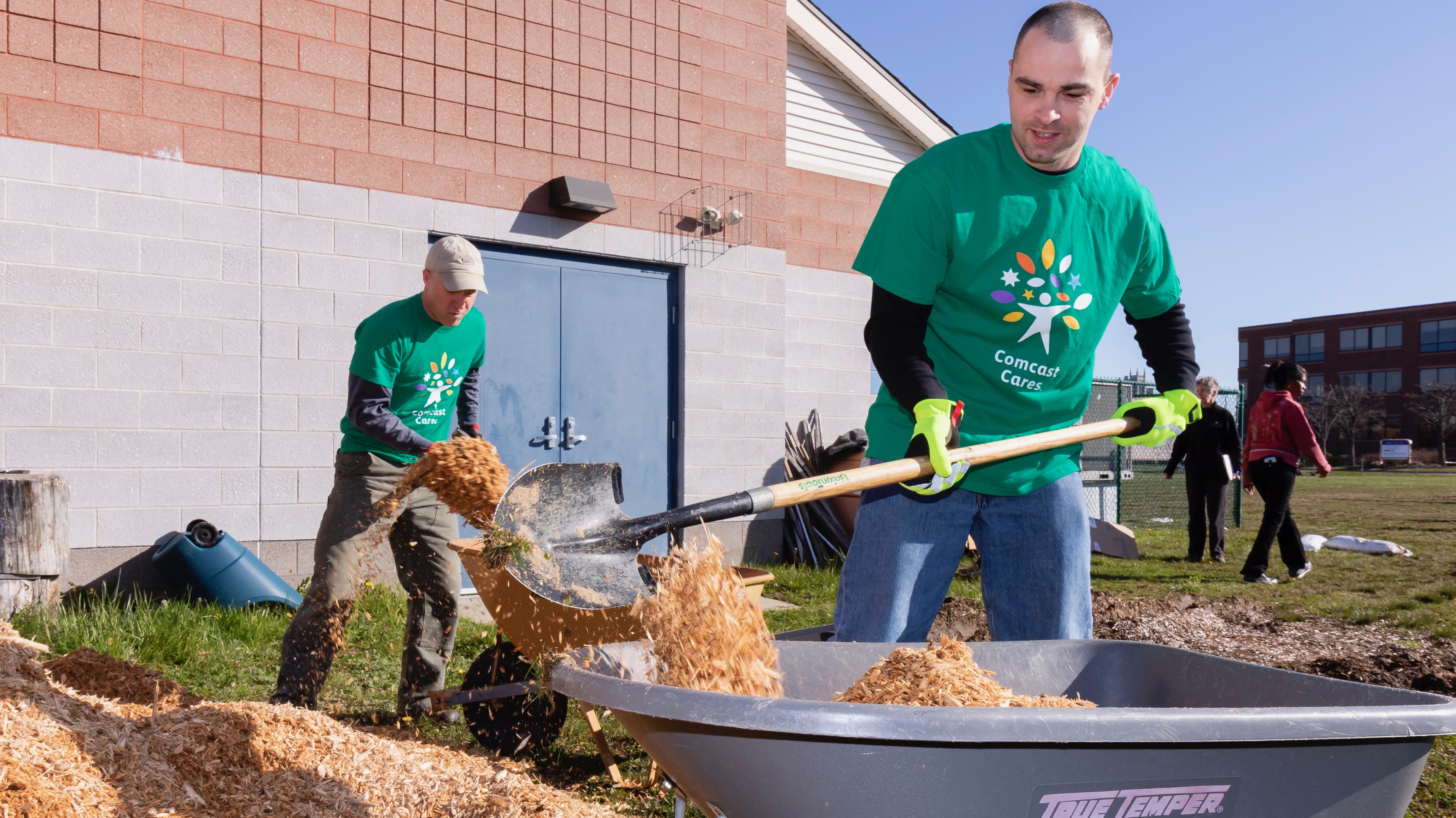 A Comcast Cares Day volunteer fills a wheelbarrow with mulch.