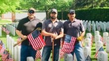 Three Xfinity employees hold American flags as they stand in a graveyard.