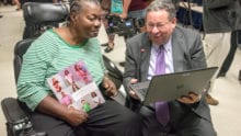 David L. Cohen presents an Internet Essentials participant with a laptop.