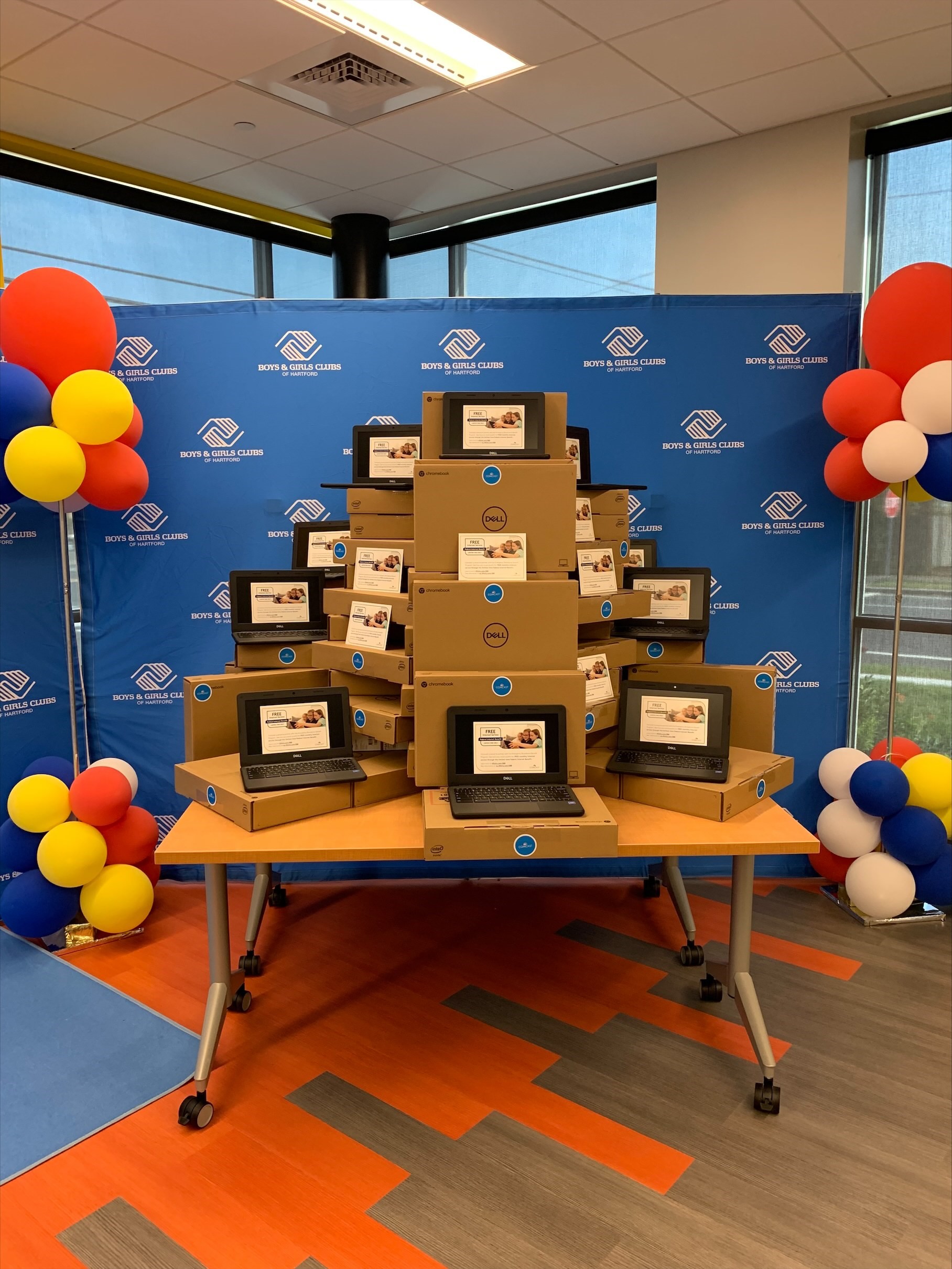 A large pile of free Internet Essentials laptops on a table during a Boys & Girls Clubs event.