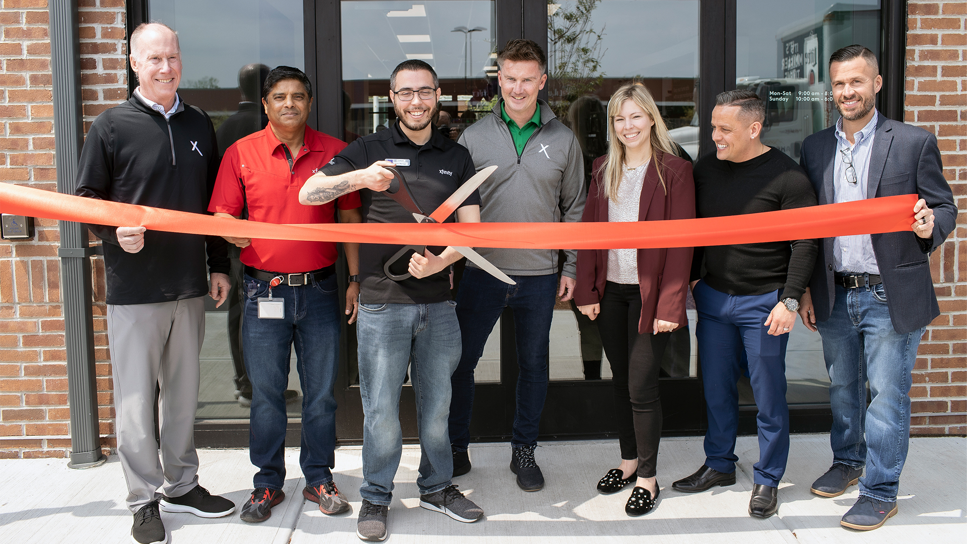 Group of smiling people posing in front of store for ribbon cutting ceremony.